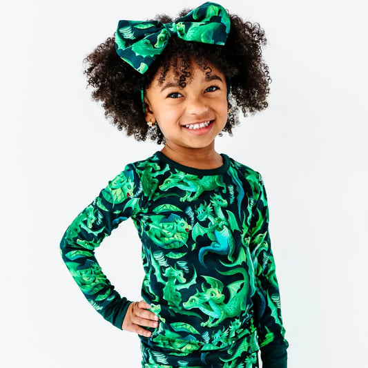 Child wearing a green dinosaur patterned outfit with a matching headband on a white background