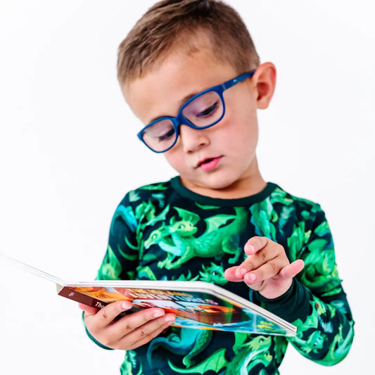 Child wearing glasses and a green dinosaur shirt, holding a tablet.