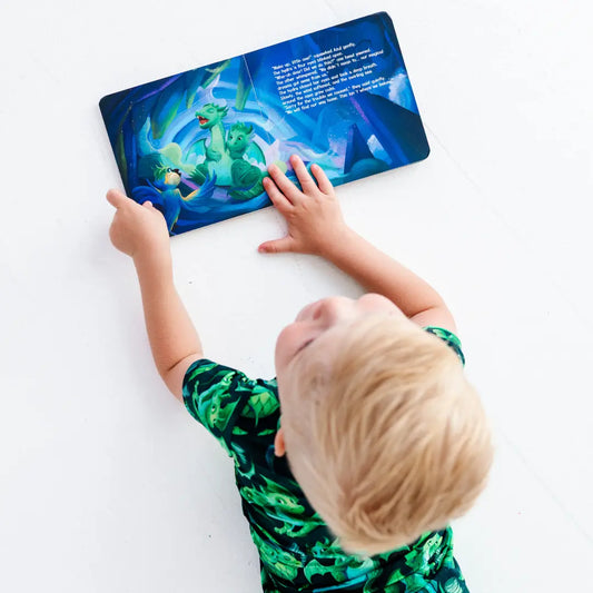 Child reading a children's book with a dragon illustration on a white surface