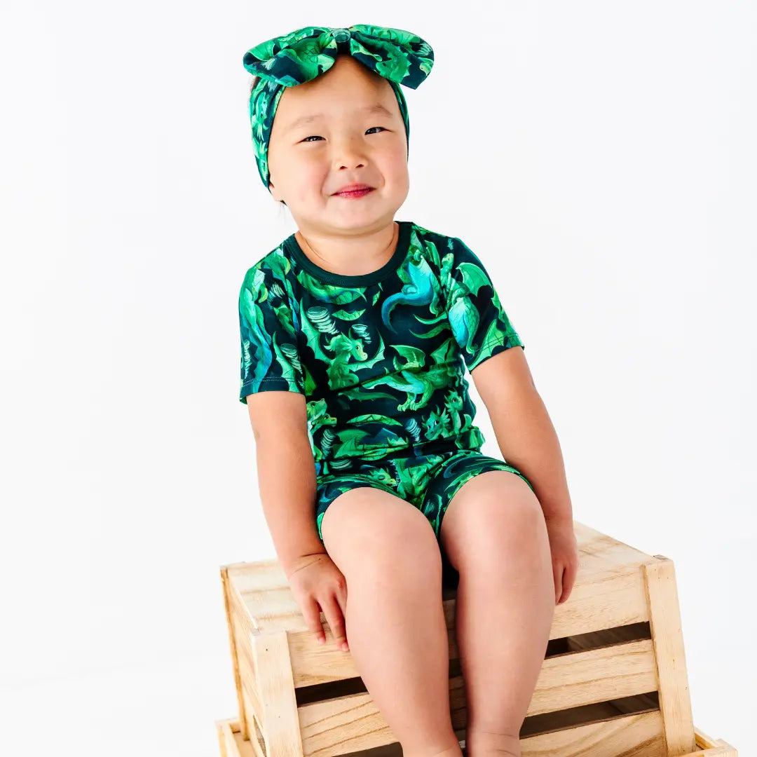 Child wearing a green camouflage outfit sitting on a wooden crate against a white background