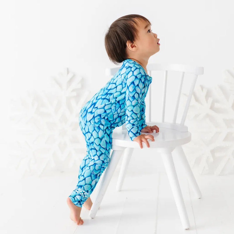 Child wearing a blue patterned onesie sitting on a white chair against a white background