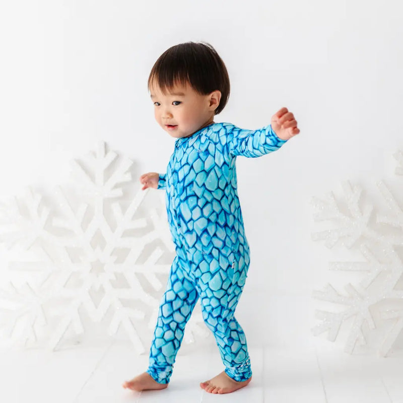 Baby wearing a blue patterned onesie standing on a white textured surface