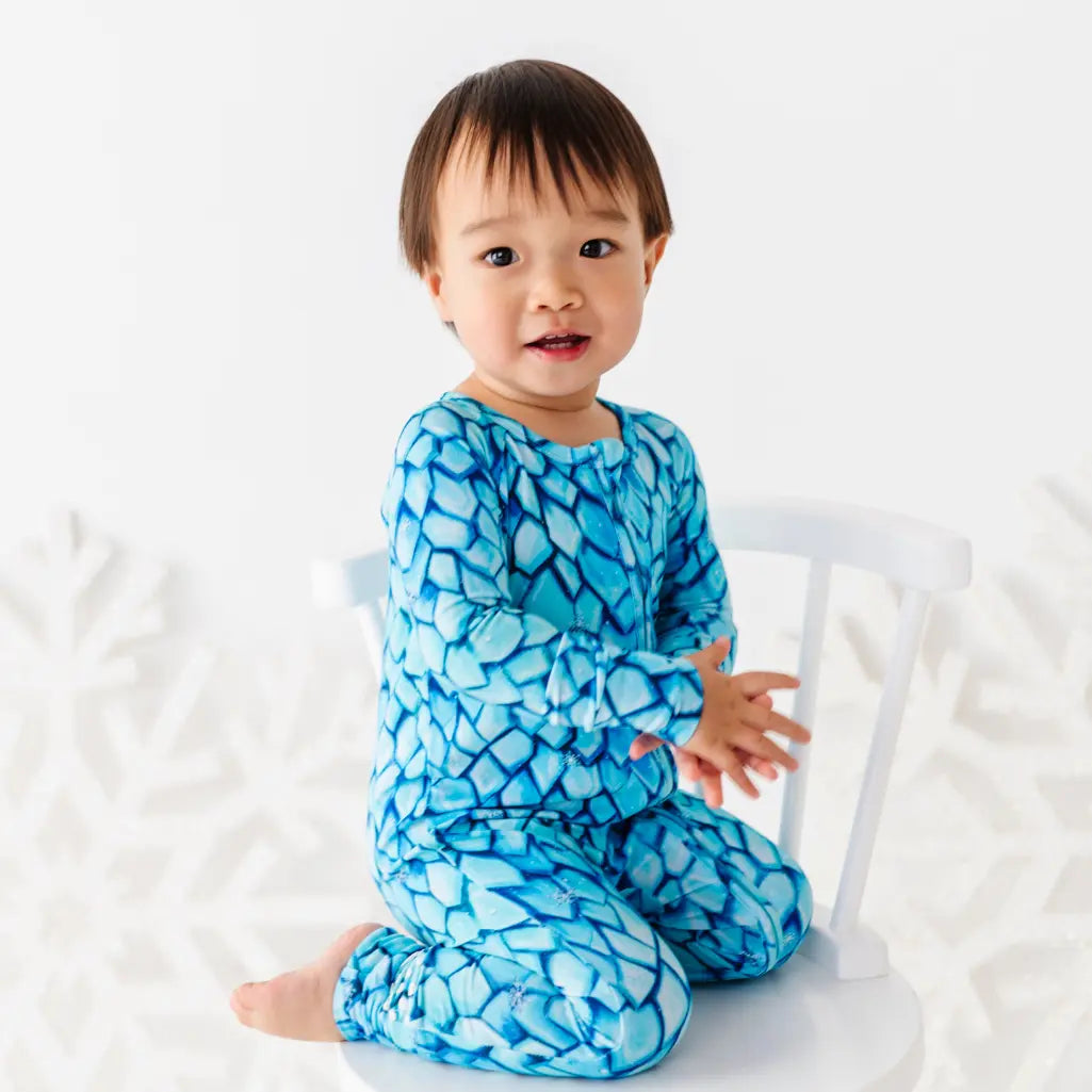 Child wearing a blue patterned outfit sitting on a white chair.