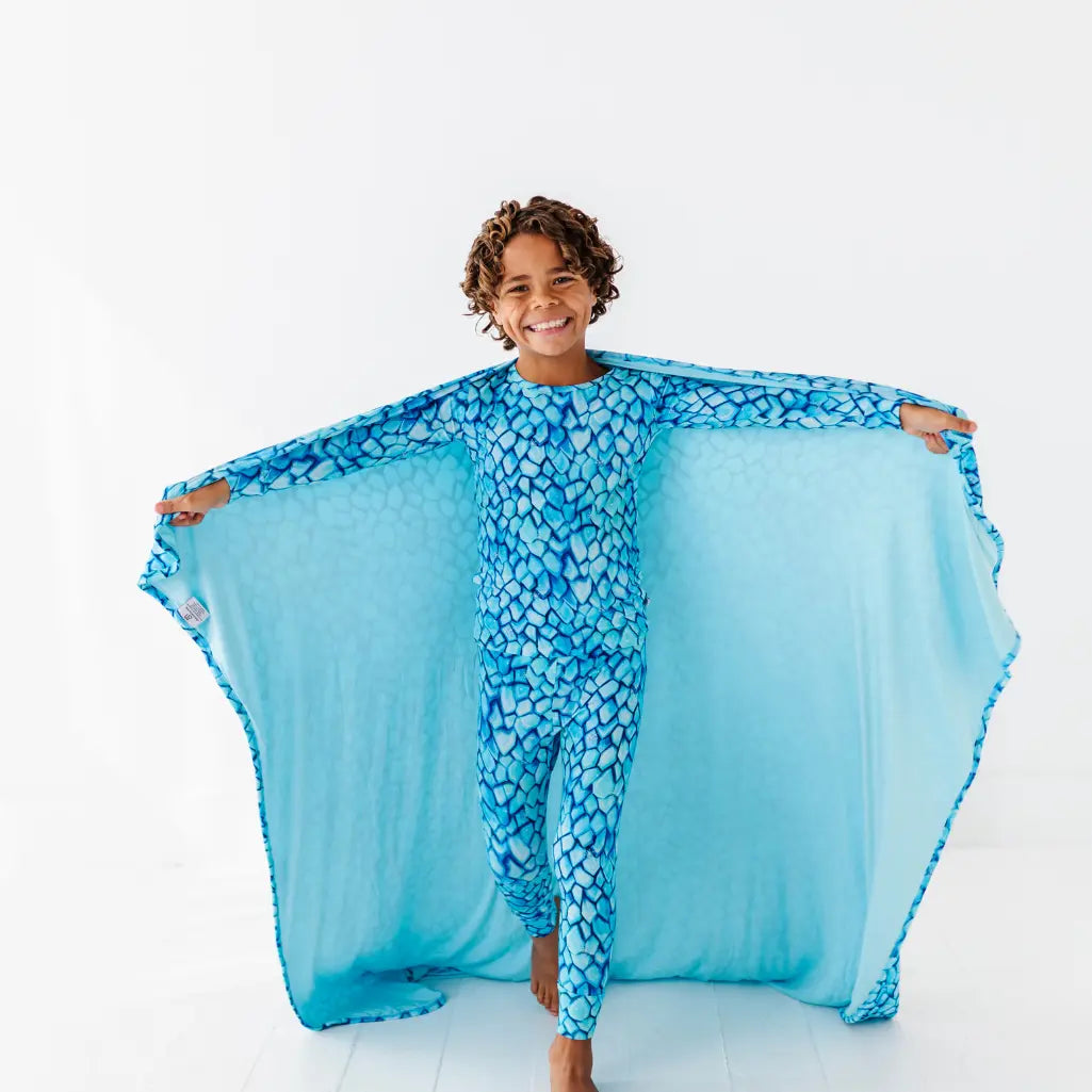 Child wearing a blue dragon costume with wings spread wide on a white background