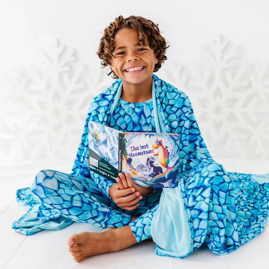 Child wearing a blue patterned onesie holding a book on a white background