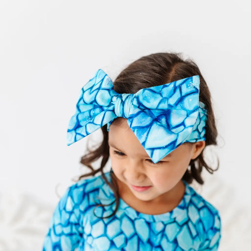Child wearing a blue patterned headband and outfit against a white background