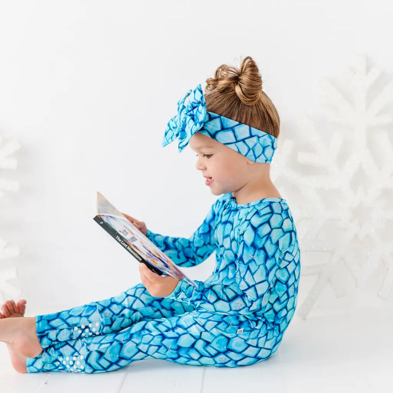 Child wearing a blue patterned outfit and headband, sitting on a white surface.