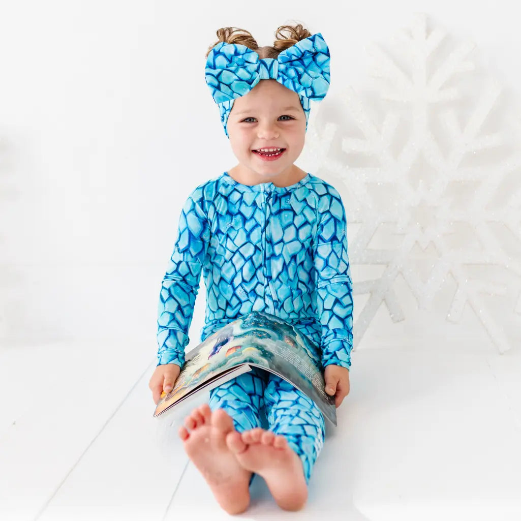 Child wearing a blue patterned outfit and headband, sitting on a white surface.