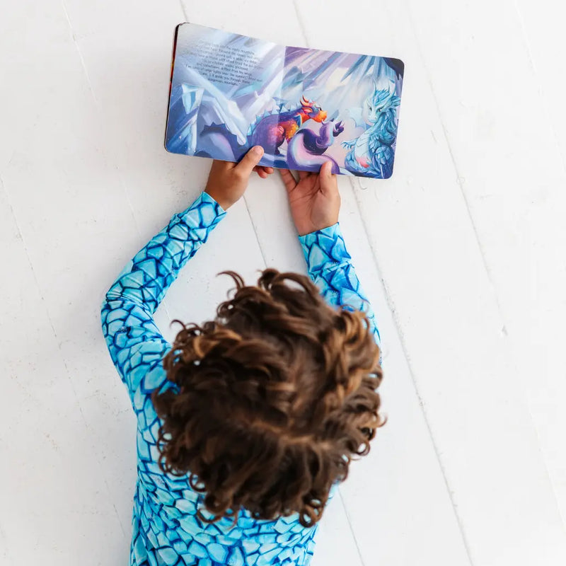 Child wearing a blue patterned shirt reading a book with a colorful cover.