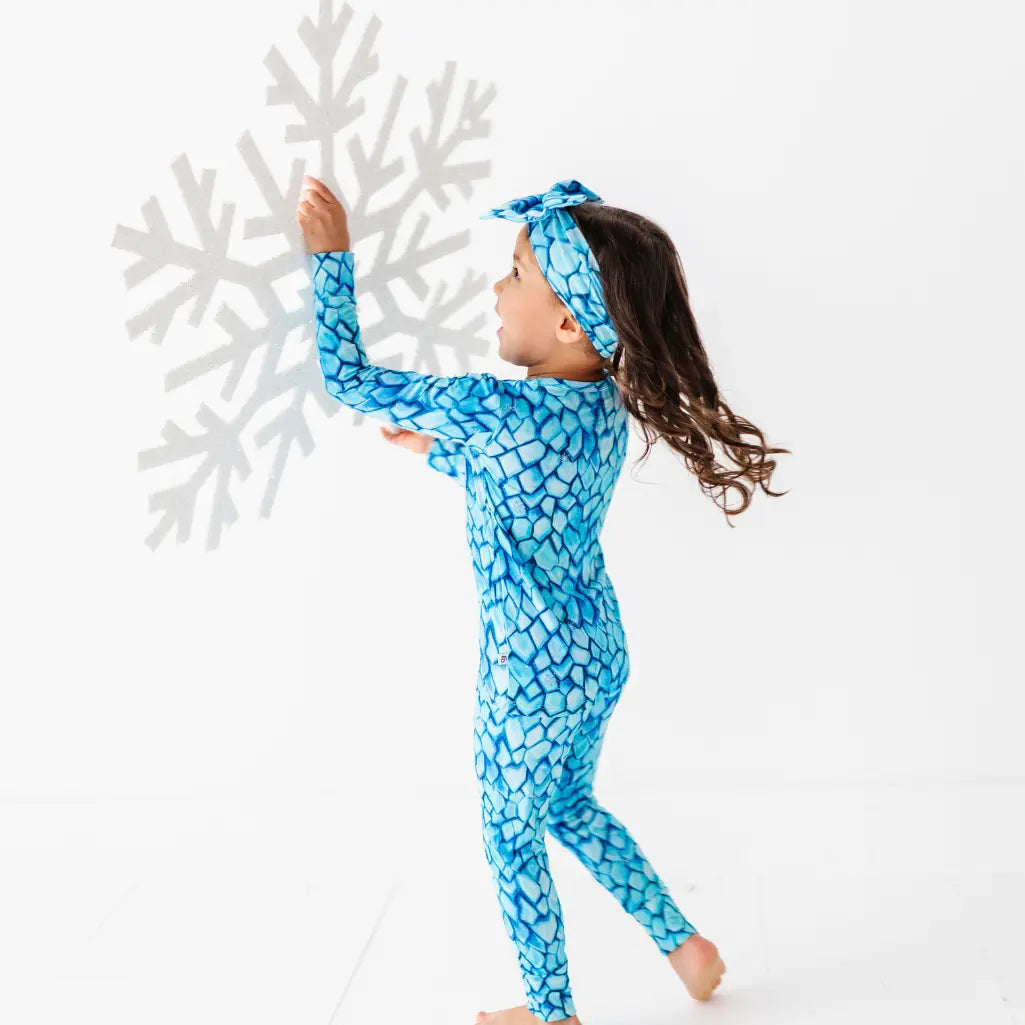 Child wearing a blue patterned onesie standing next to a large white snowflake.