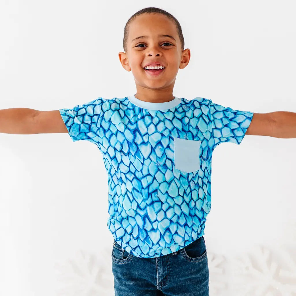 Child wearing a blue patterned shirt with arms outstretched on a white background