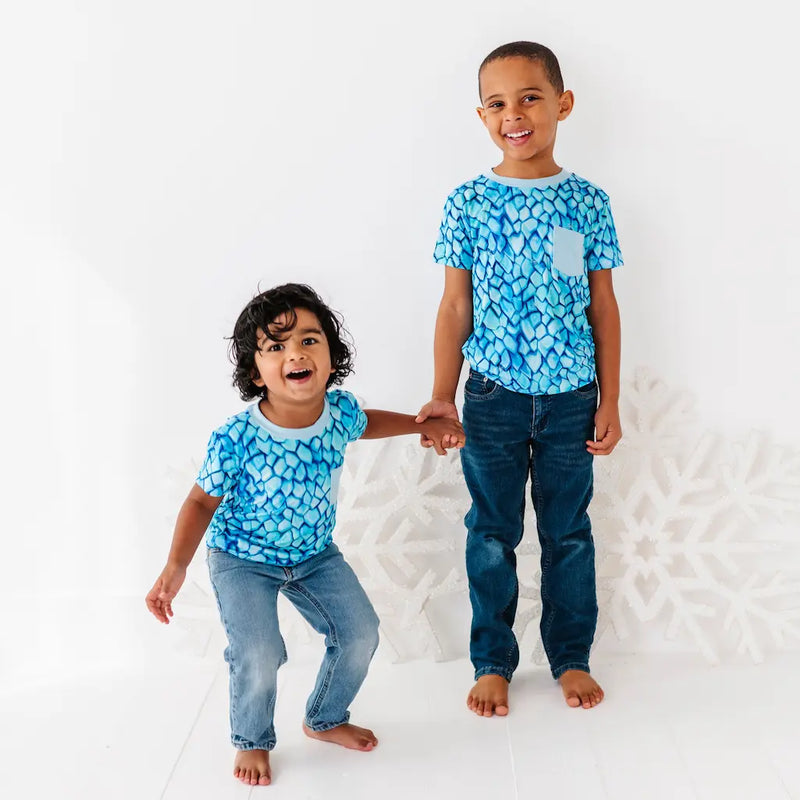 Two children wearing matching blue patterned shirts and jeans standing against a white background.