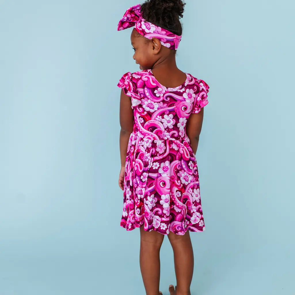 Young girl wearing a pink floral octopus-themed dress and headband on a light blue background