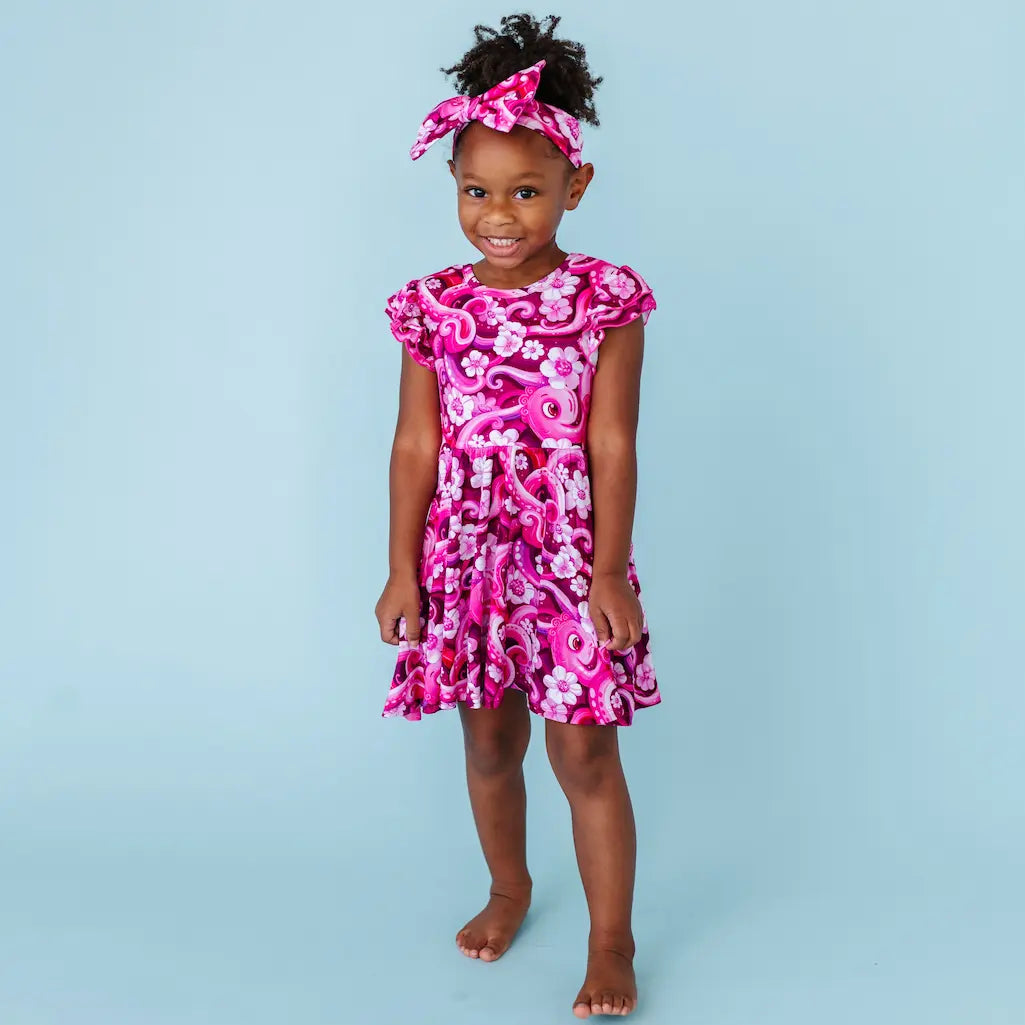 Young girl wearing a pink floral octopus-themed dress against a light blue background
