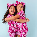 Two children wearing pink outfits with floral patterns against a light blue background