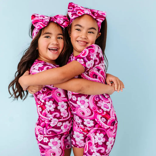 Two children wearing pink outfits with floral patterns against a light blue background