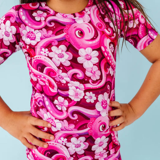 Child wearing a pink and purple floral and octopus patterned shirt against a light blue background