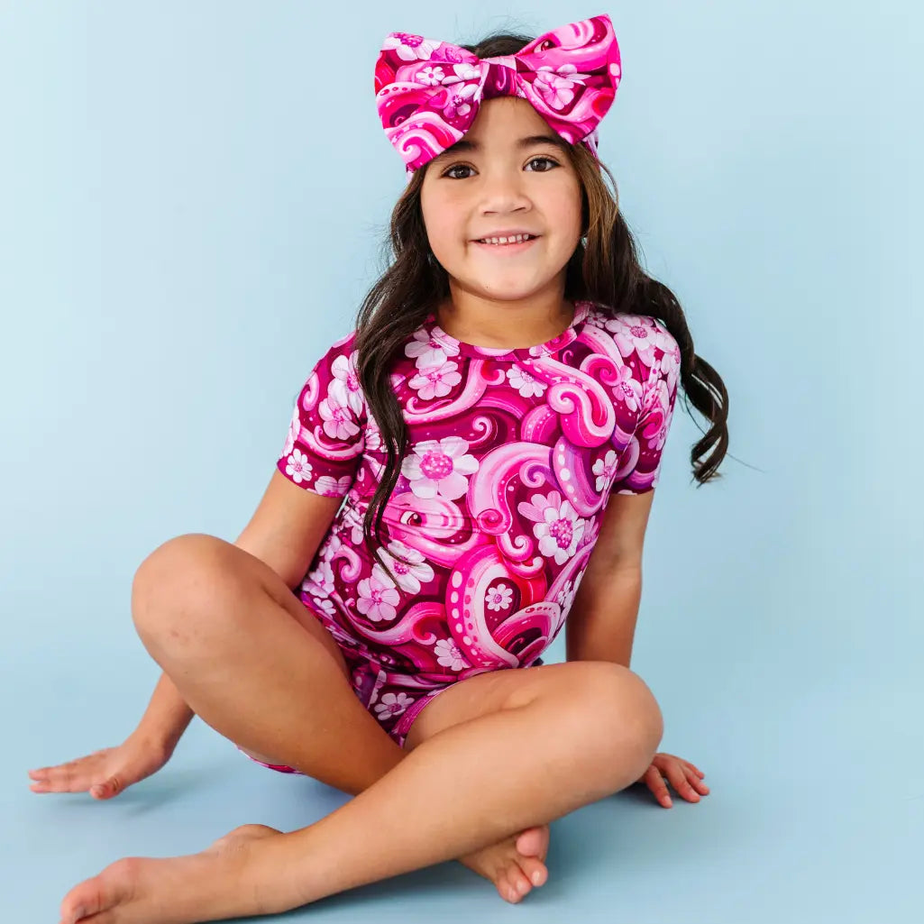 Young girl wearing a pink and white patterned outfit with a matching headband on a light blue background