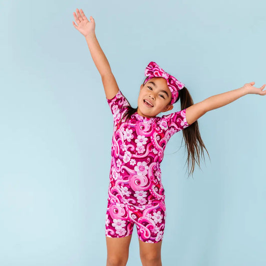 Child wearing a pink and white patterned swimsuit with arms raised against a light blue background
