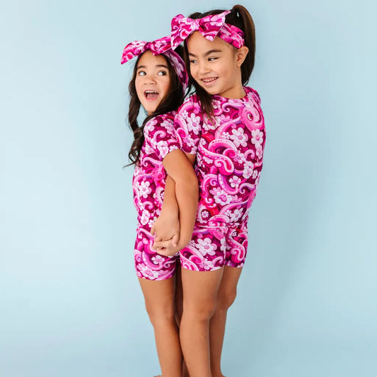 Two children wearing matching pink floral outfits against a light blue background