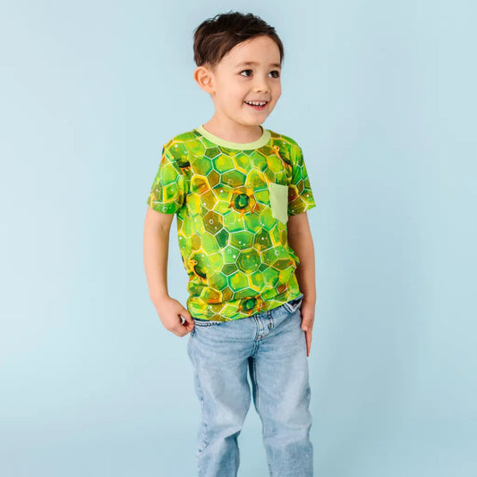 Child wearing a green and yellow patterned shirt with blue jeans on a light blue background