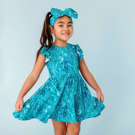 Young girl wearing a blue dress with a matching headband against a light blue background