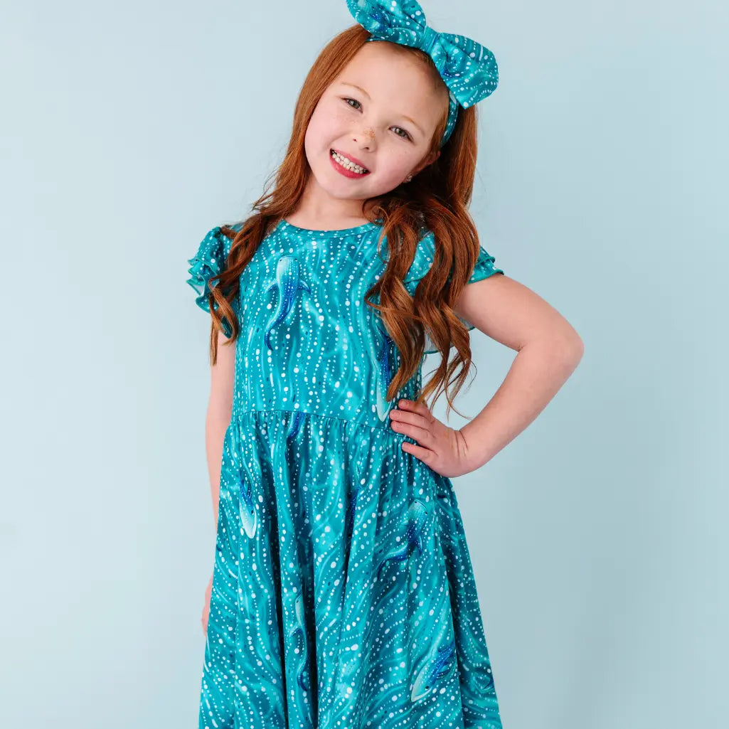 Young girl wearing a blue dress with a pattern, standing against a light blue background