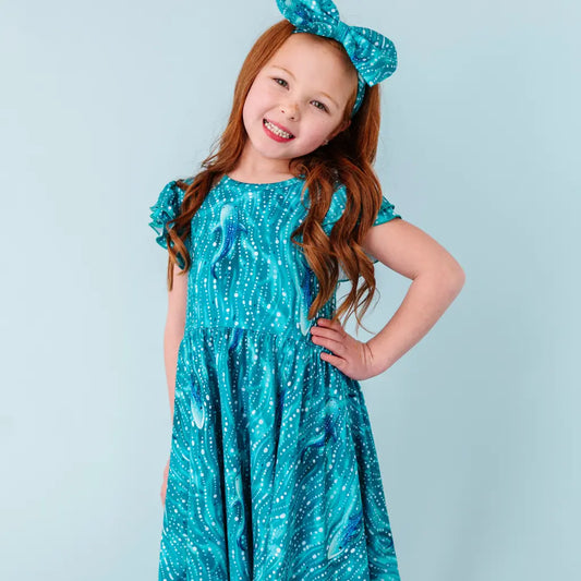 Young girl wearing a blue dress with a pattern, standing against a light blue background