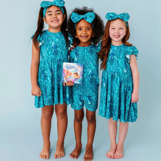 Three children wearing matching blue sequin dresses against a light blue background