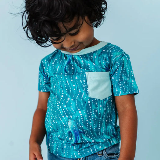 Child wearing a teal whale shark patterned t-shirt with a white pocket on a light blue background