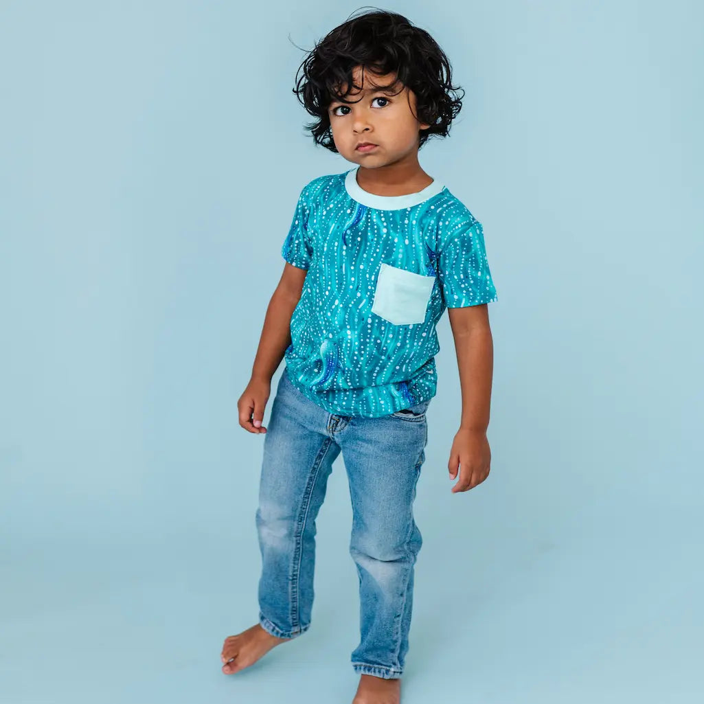 Young child wearing a teal whale shark patterned t-shirt with jeans on a light blue background