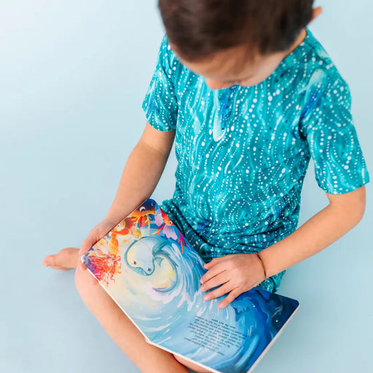 Child wearing a blue sequin outfit holding a colorful book against a light blue background