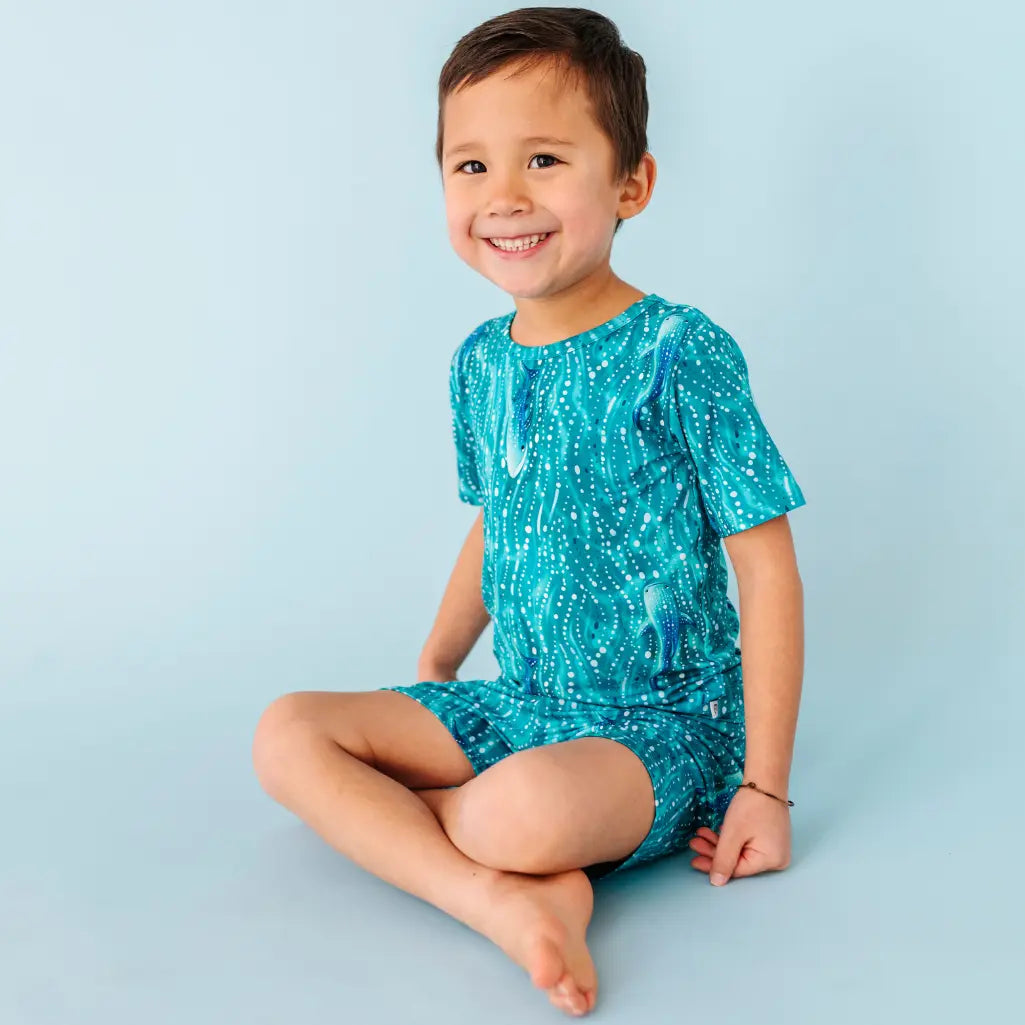 Child wearing a blue patterned outfit sitting on a light blue background