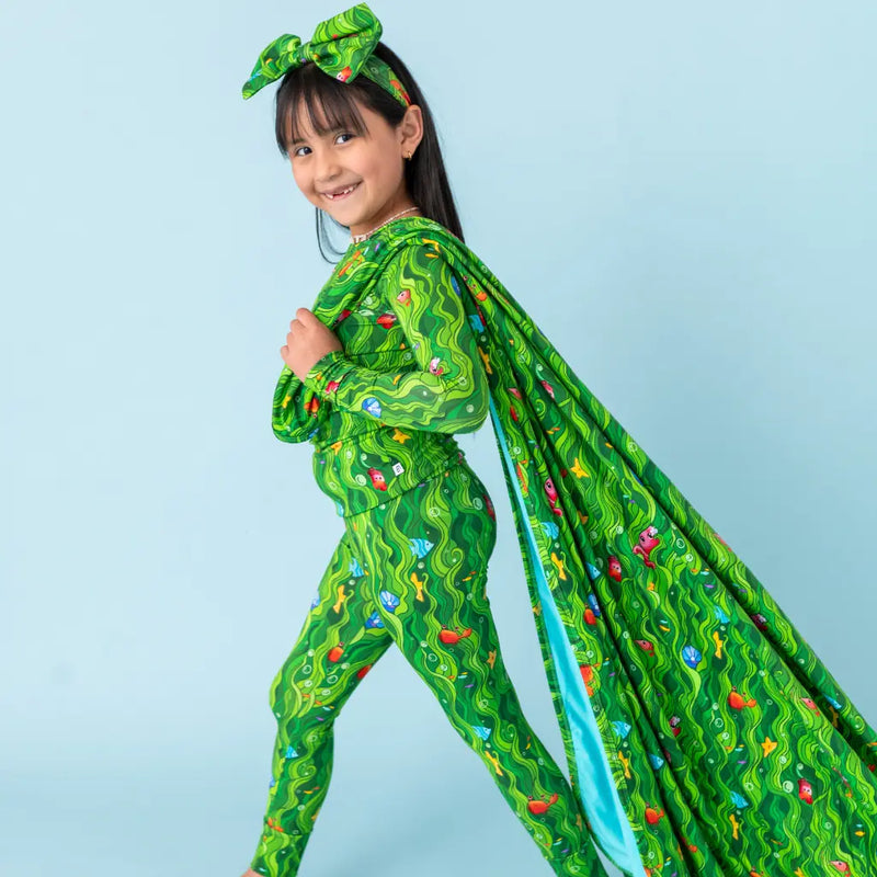 Child wearing a green superhero costume with a cape on a light blue background
