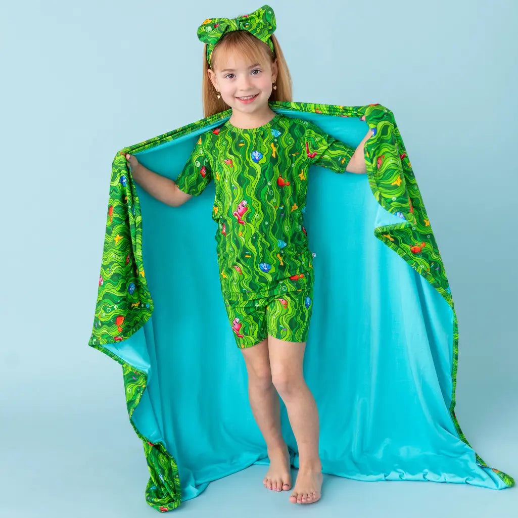 Child wearing a green dinosaur-themed outfit with a matching cape against a light blue background