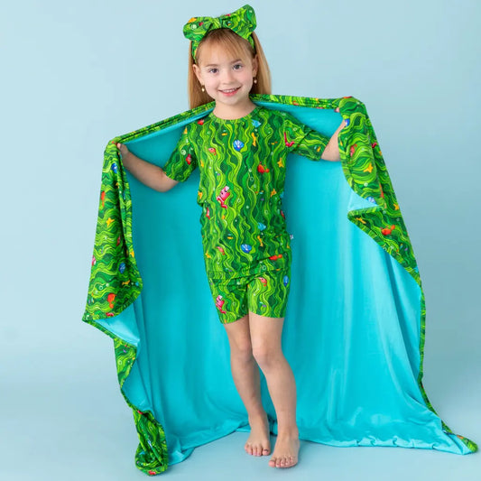 Child wearing a green dinosaur-themed outfit with a matching cape against a light blue background