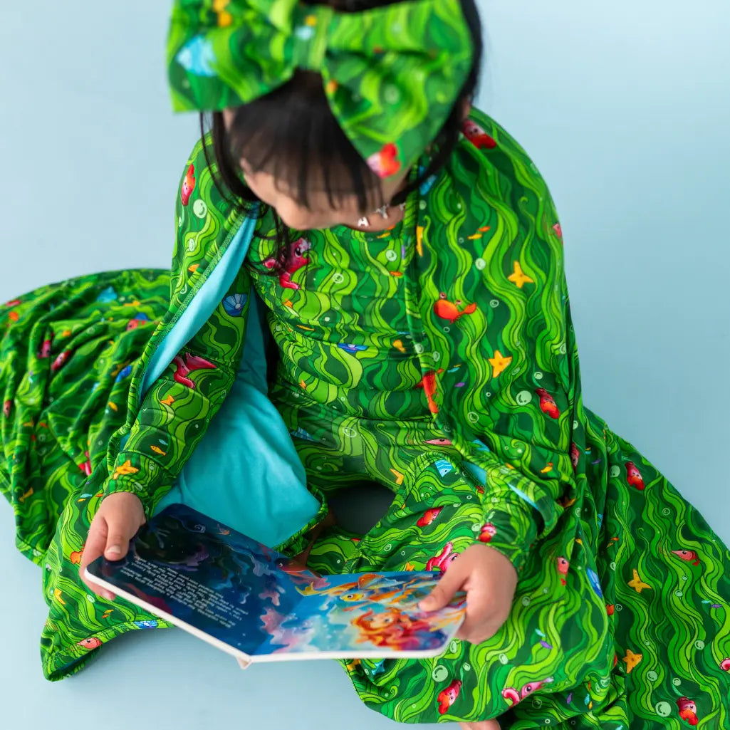 Child wearing a green patterned outfit holding a phone on a light blue background