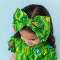 Child wearing a green patterned headband and outfit against a light blue background
