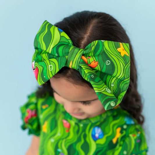 Child wearing a green patterned headband and outfit against a light blue background