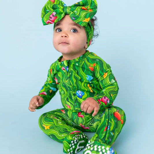 Child wearing a green patterned outfit and headband on a light blue background