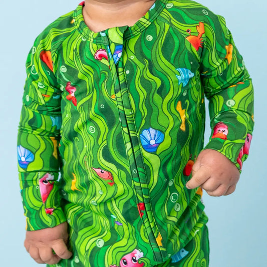 Child wearing a green patterned shirt with fish and shell design on a light blue background