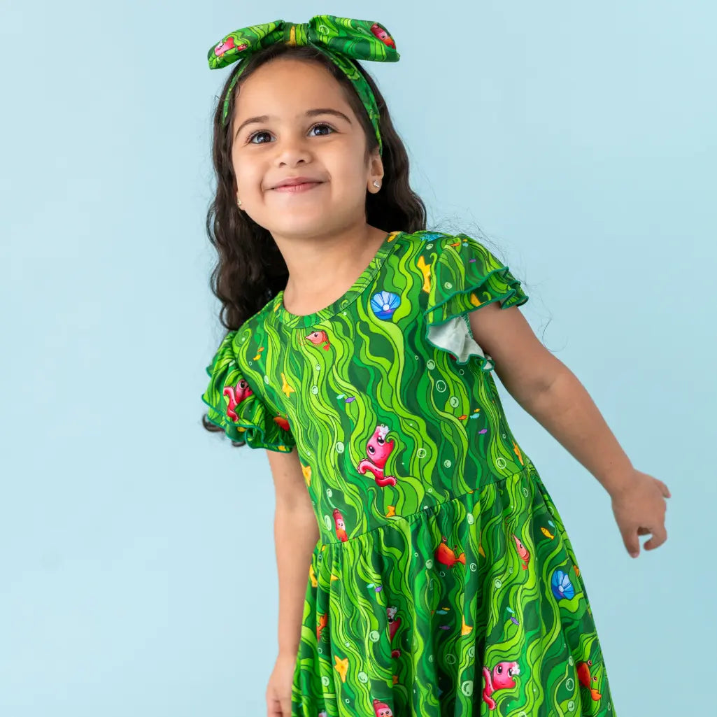 Child wearing a green patterned dress against a light blue background