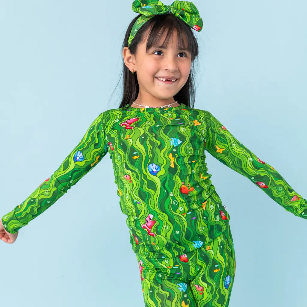 Child wearing a green patterned outfit with a matching headband on a light blue background