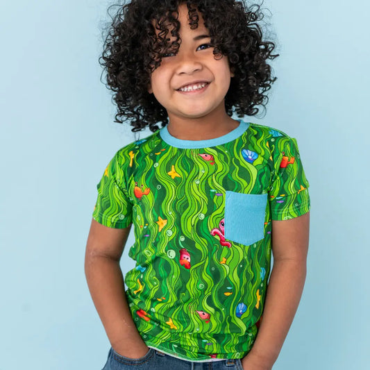 Child wearing a green patterned shirt with a blue pocket on a light blue background