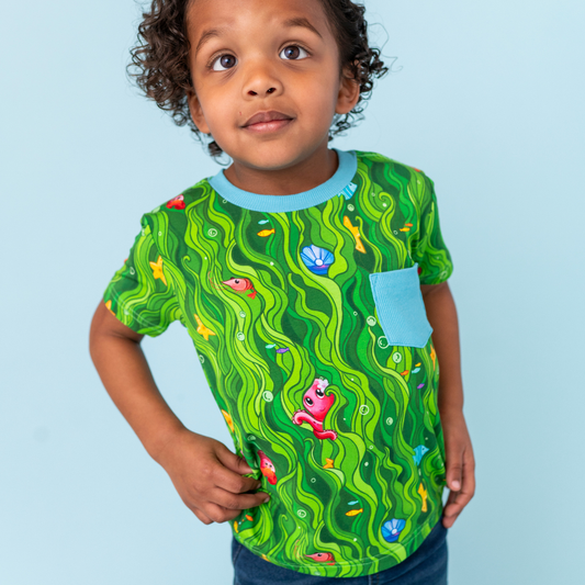 Child wearing a green t-shirt with colorful patterns on a light blue background