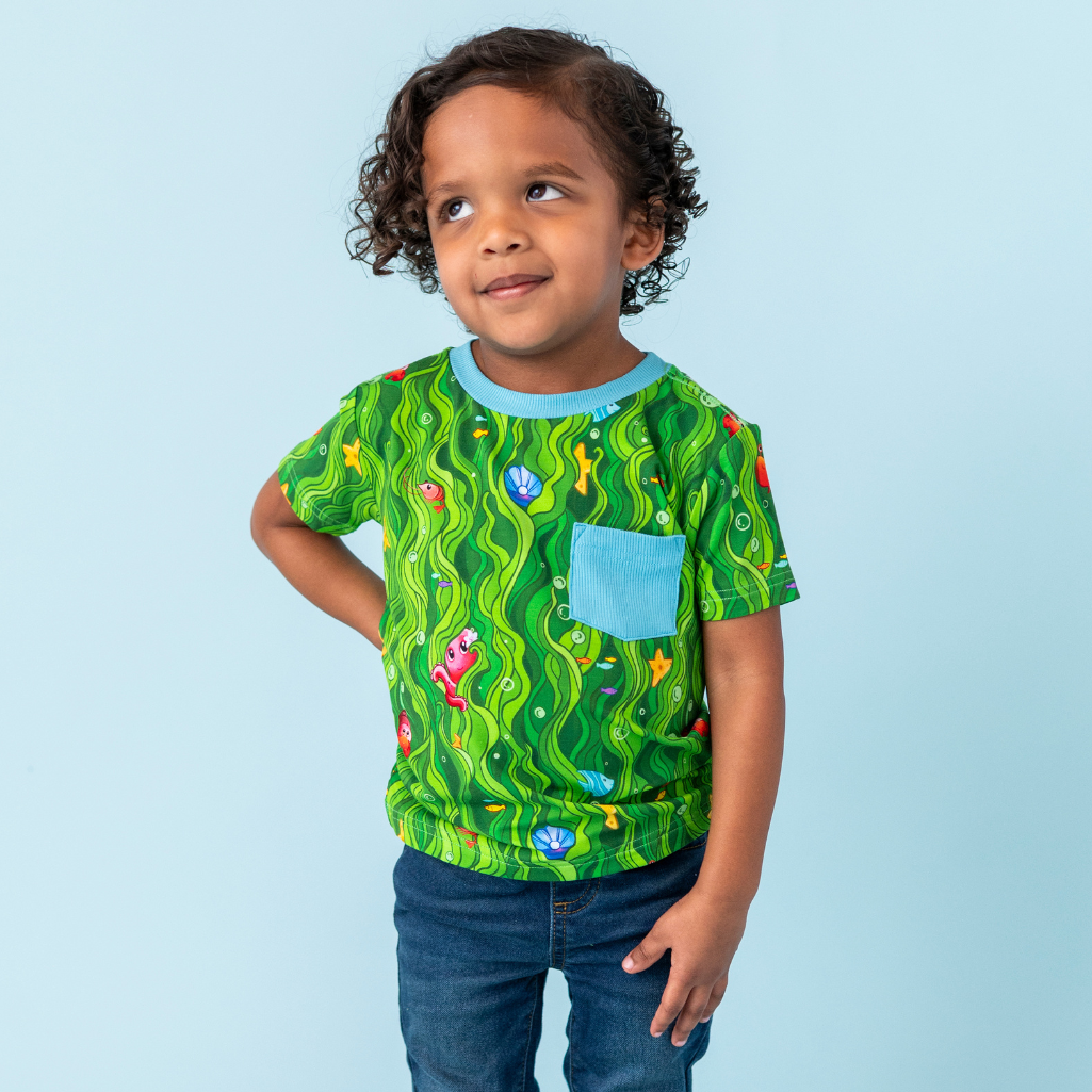 Child wearing a green patterned shirt with a blue pocket on a light blue background