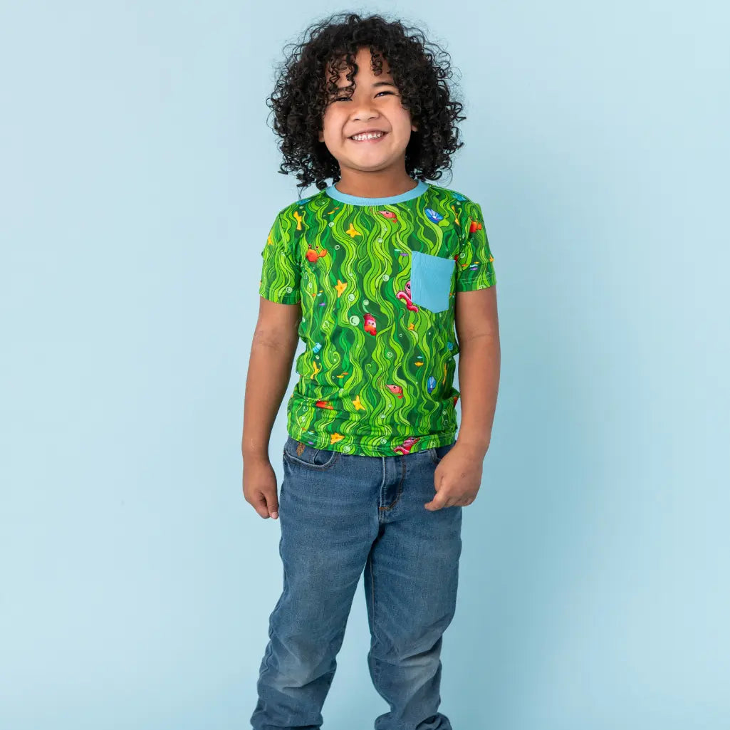 Child wearing a green patterned shirt with a blue pocket against a light blue background