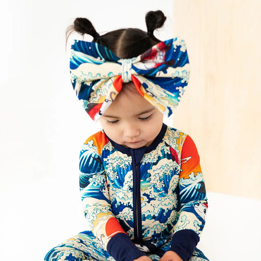 Child wearing a colorful outfit with a headband featuring a large bow.