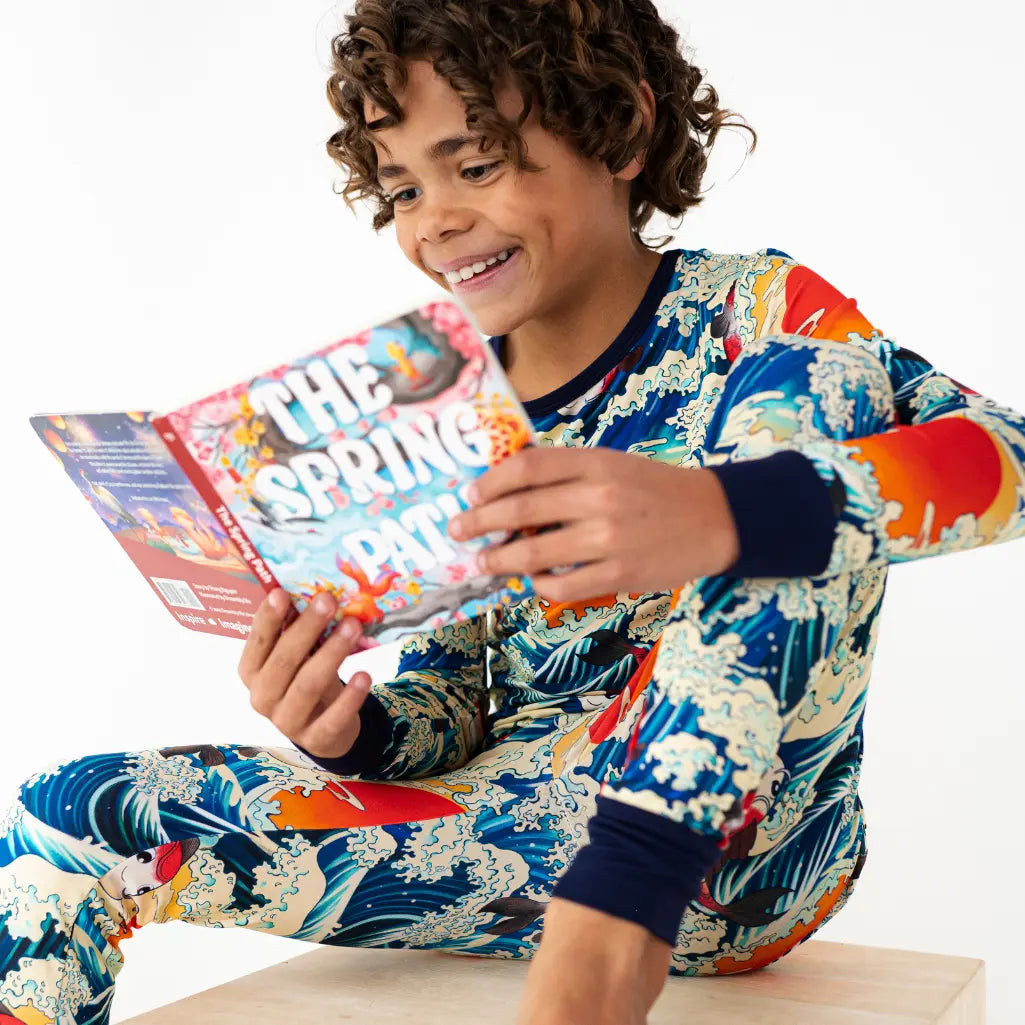 Child wearing colorful pajamas reading a book with a white background