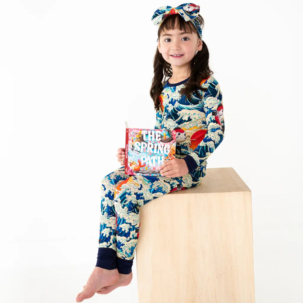 Child wearing a colorful dragon-themed pajama set holding a book on a white background